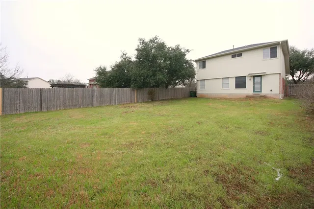 a view of a white house in front of a yard with wooden fence
