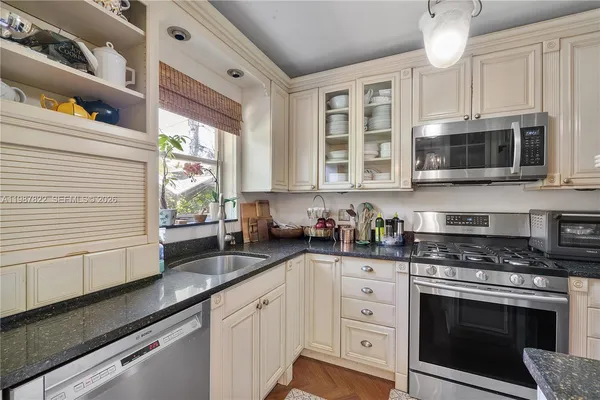 a kitchen with granite countertop white cabinets stainless steel appliances a sink and a window