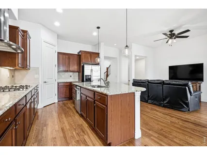 a kitchen with stainless steel appliances granite countertop a stove top oven a sink dishwasher and a refrigerator with wooden floor