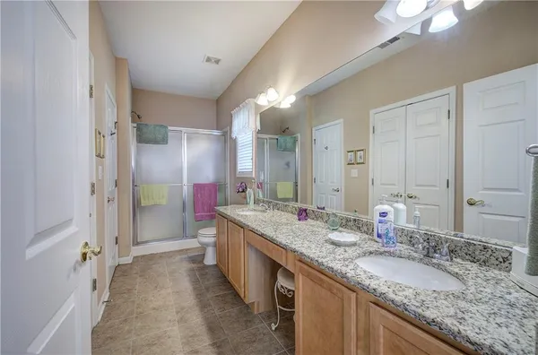 a bathroom with a granite countertop double vanity sink and mirror with shower