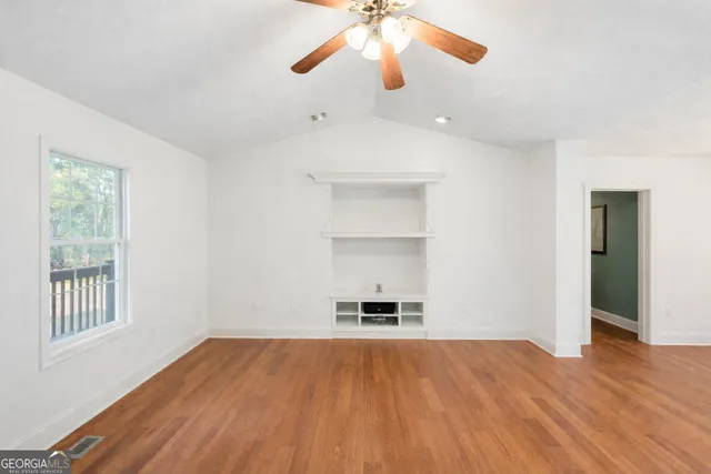 a view of empty room with wooden floor and fan