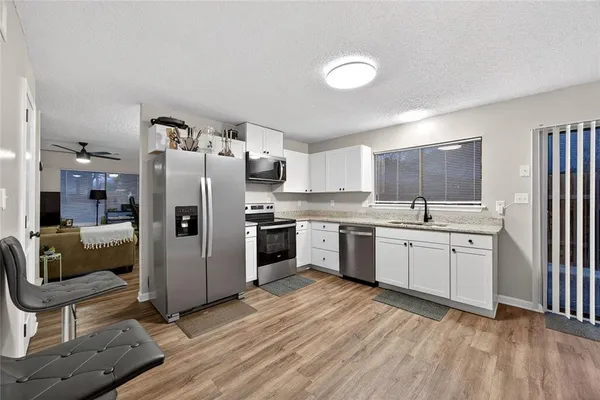 a kitchen with granite countertop a refrigerator a sink dishwasher and white cabinets with wooden floor