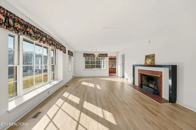 a view of an empty room with wooden floor fireplace and a window
