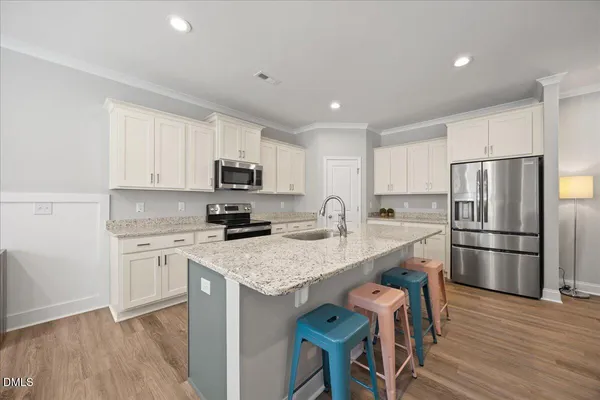 a kitchen with stainless steel appliances a refrigerator a stove a sink dishwasher and white cabinets with wooden floor