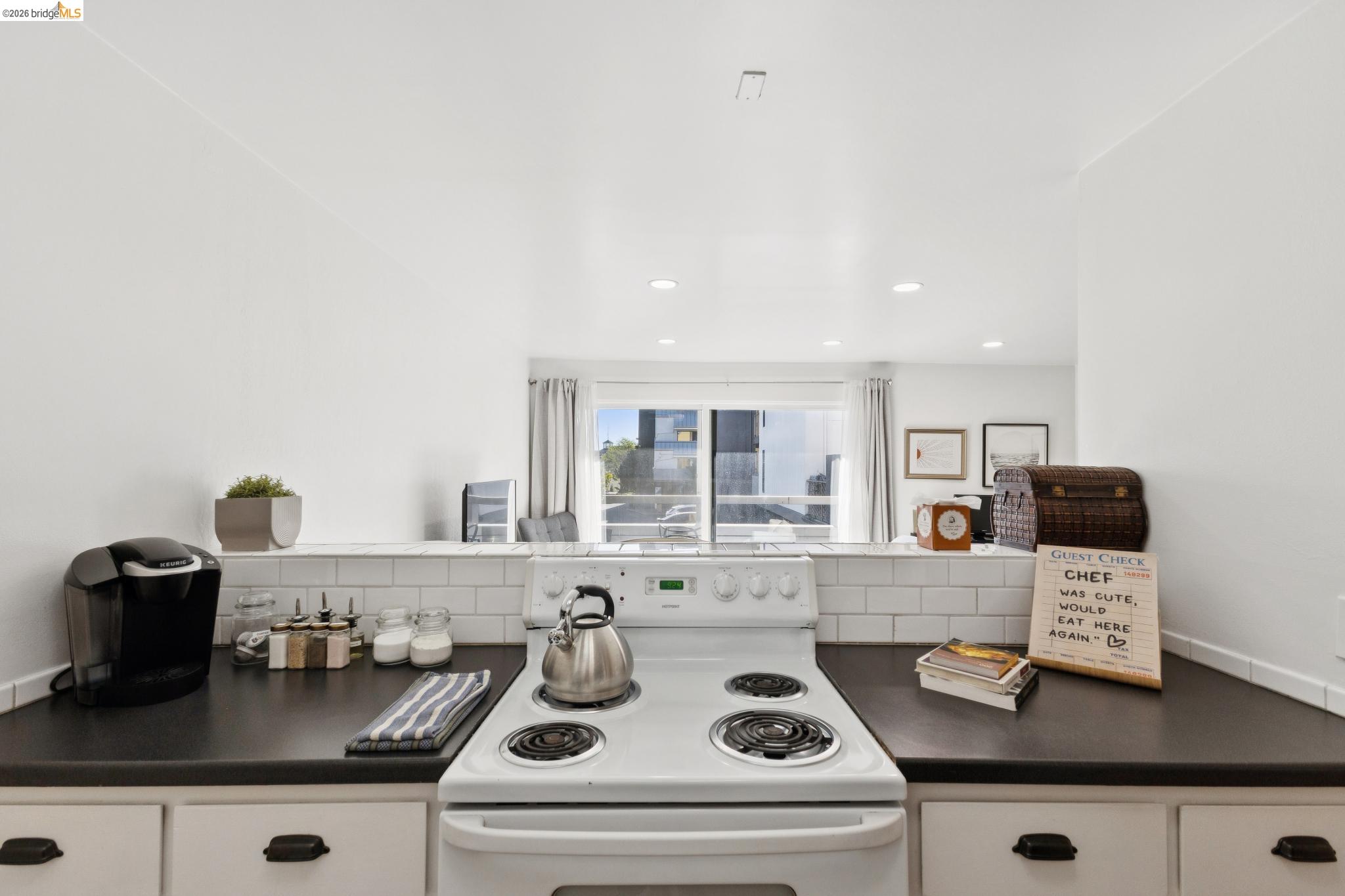 5 Embarcadero, Unit 129 Oakland, CA 94607 - Photo 3 of 32 Kitchen with dark countertops, white electric range oven, white cabinets, and backsplash