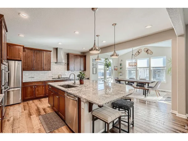 a open kitchen with stainless steel appliances granite countertop a stove top oven a refrigerator and white cabinets with wooden floor