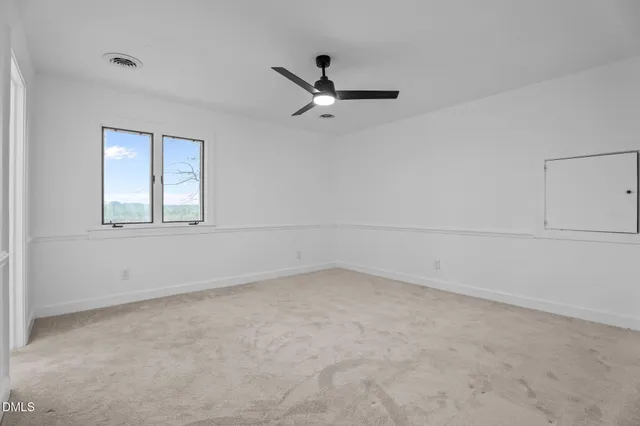 an empty room with chandelier fan and windows