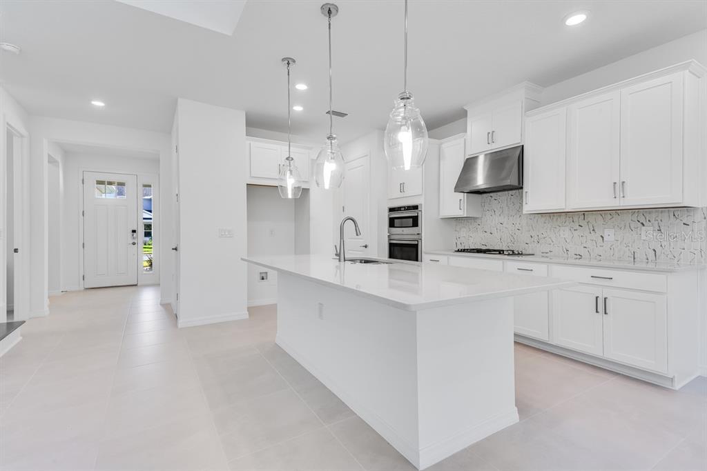 581 Moon Shell Circle New Smyrna Beach, FL 32168 - Photo 7 of 40 a large white kitchen with stainless steel appliances kitchen island granite countertop a refrigerator a stove a sink and white cabinets