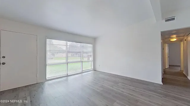 a view of an empty room with wooden floor and a window