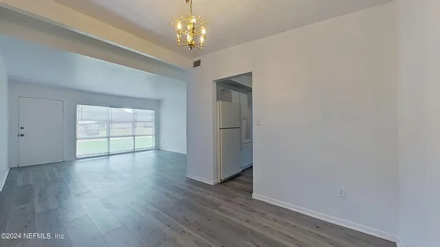 an empty room with wooden floor chandelier and windows