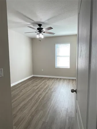 an empty room with wooden floor chandelier fan and windows