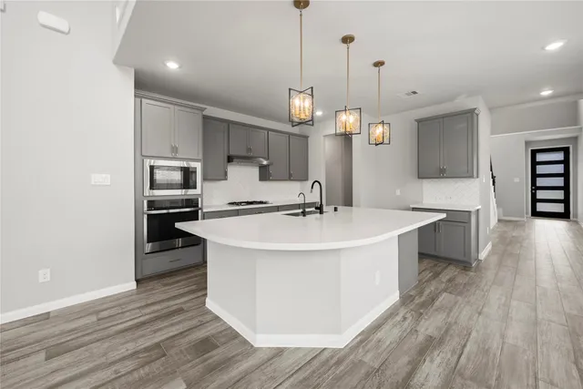 a kitchen with stainless steel appliances a sink a stove a refrigerator and island with wooden floor