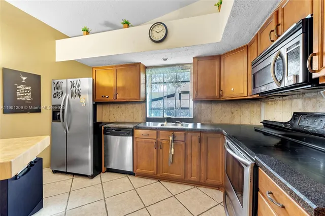 a kitchen with stainless steel appliances granite countertop a sink a stove a refrigerator a washer dryer and cabinets