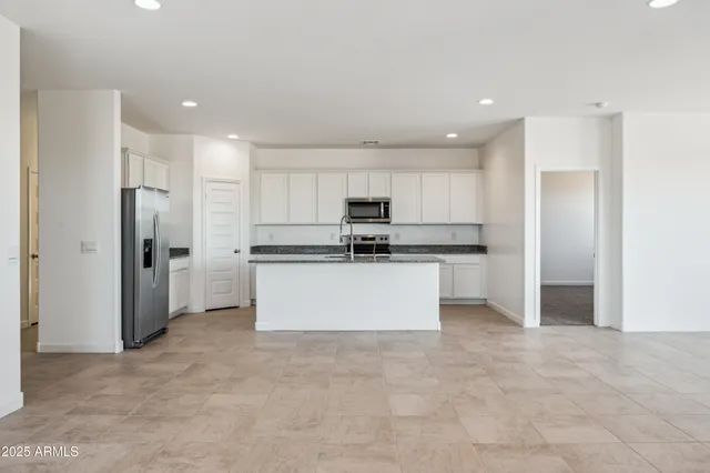 a large kitchen with stainless steel appliances a refrigerator and white cabinets
