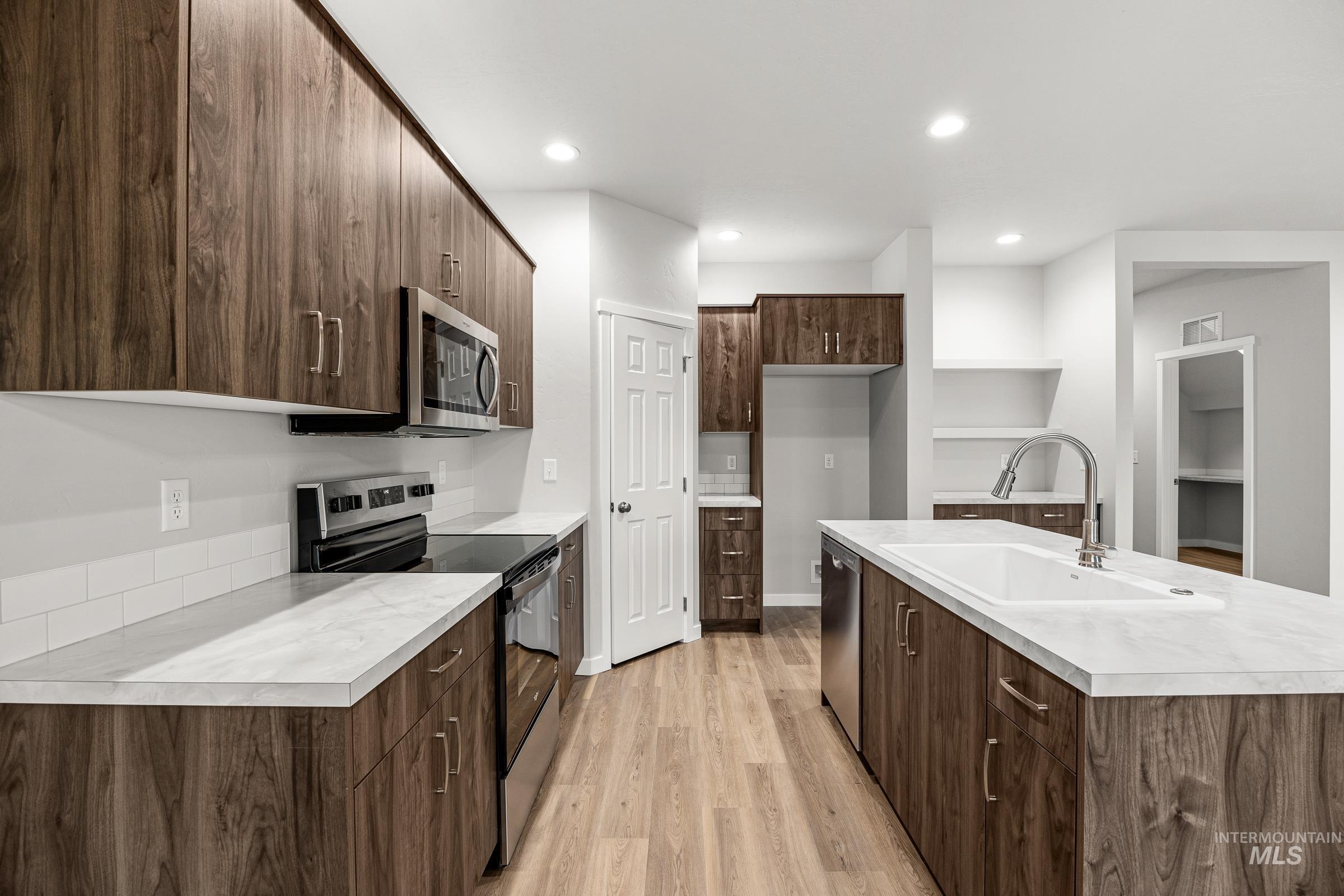 13656 Redway Court Caldwell, ID 83607 - Photo 6 of 21 Modern kitchen featuring stainless steel appliances, wood-finish cabinetry, light-toned countertops, an island with a matching countertop, and recessed lighting