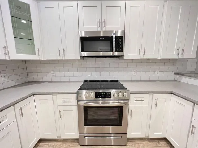 a kitchen with stainless steel appliances granite countertop white cabinets and a stove a oven with wooden floor
