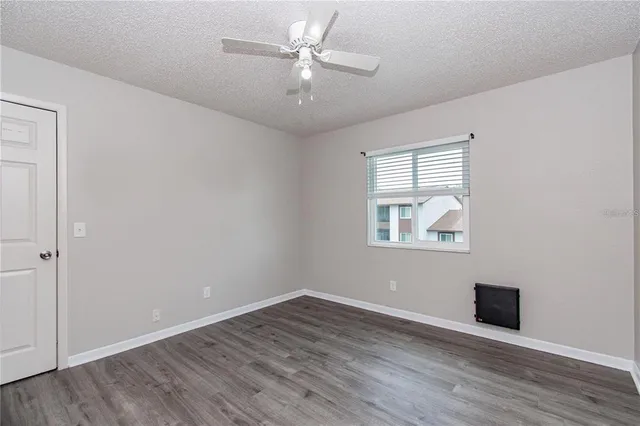 an empty room with wooden floor chandelier fan and windows