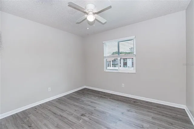 an empty room with wooden floor ceiling fan and windows
