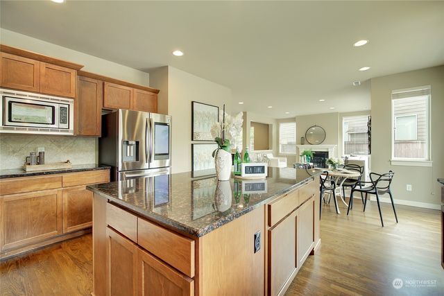 a kitchen with stainless steel appliances granite countertop a stove top oven a refrigerator a dining table and chairs with wooden floor