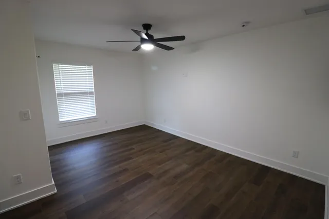 an empty room with wooden floor ceiling fan and windows