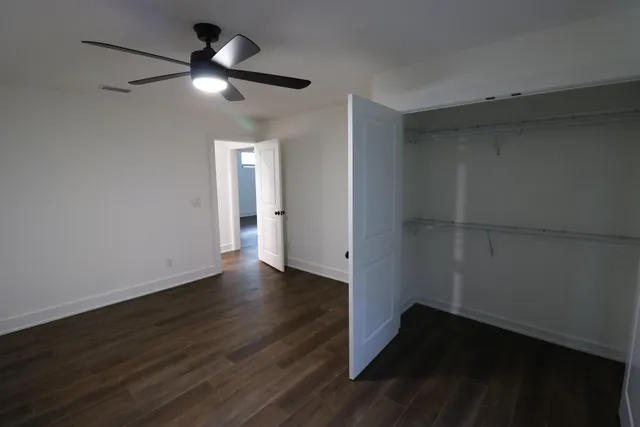an empty room with wooden floor fan and windows