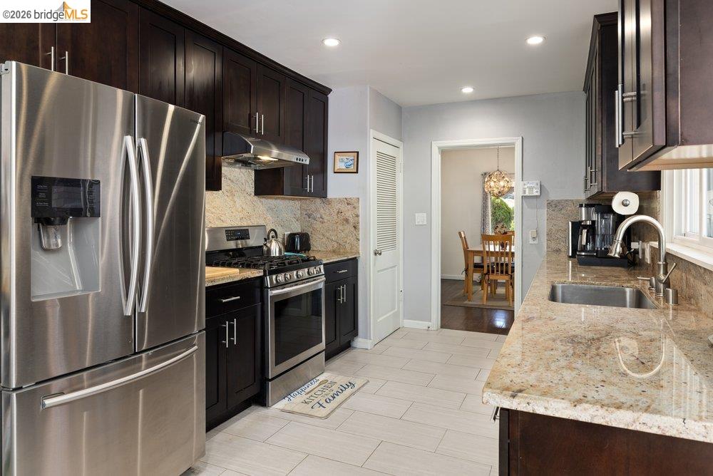 9600 Golf Links Road Oakland, CA 94605 - Photo 37 of 47 Kitchen with appliances with stainless steel finishes, light stone counters, under cabinet range hood, dark brown cabinets, and recessed lighting
