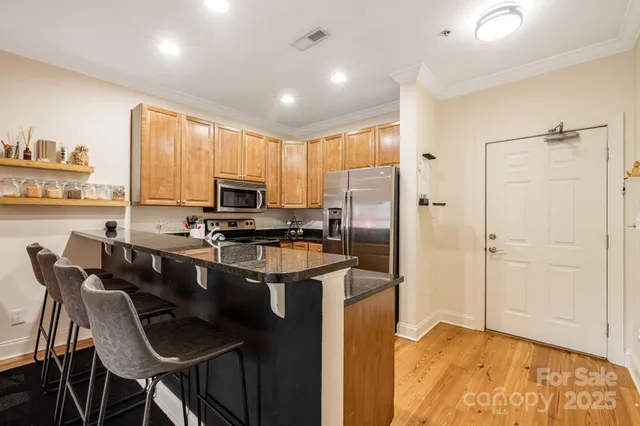 a kitchen with stainless steel appliances granite countertop a stove top oven a sink a refrigerator with a dining table and chairs with wooden floor