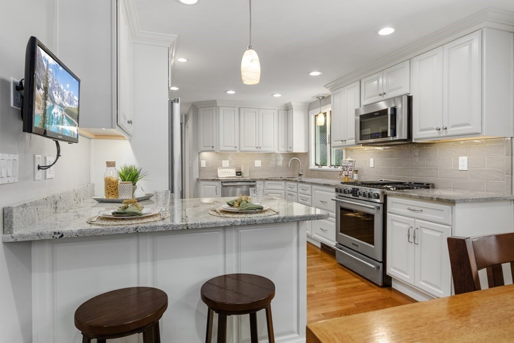 25 Oak Street Reading, MA 01867 - Photo 10 of 42 a kitchen with stainless steel appliances granite countertop a sink a stove a microwave a refrigerator and white cabinets