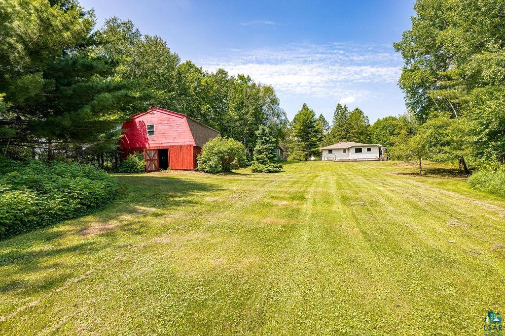 2592 Strandberg Road Barnum, MN 55707 - Photo 26 of 44 Expansive green lawn with a red barn featuring a gable roof and double barn doors, surrounded by mature trees