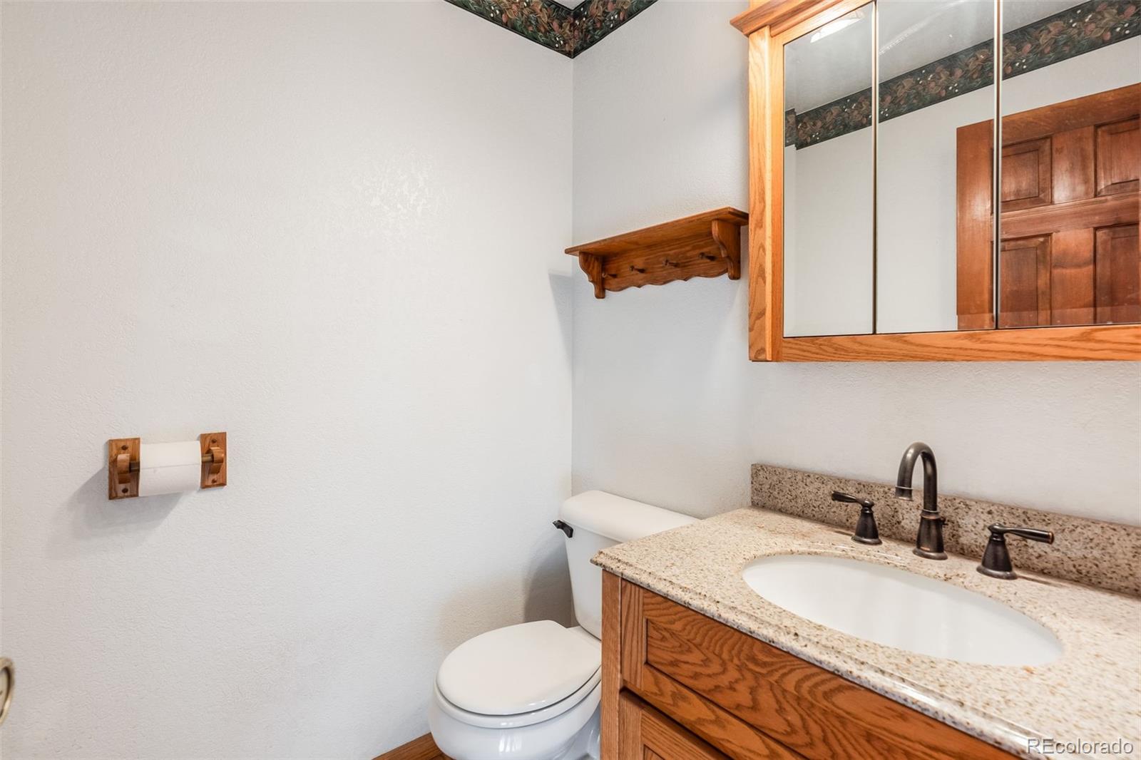 7572 Surrey Drive Morrison, CO 80465 - Photo 19 of 38 a bathroom with a granite countertop sink a toilet and mirror