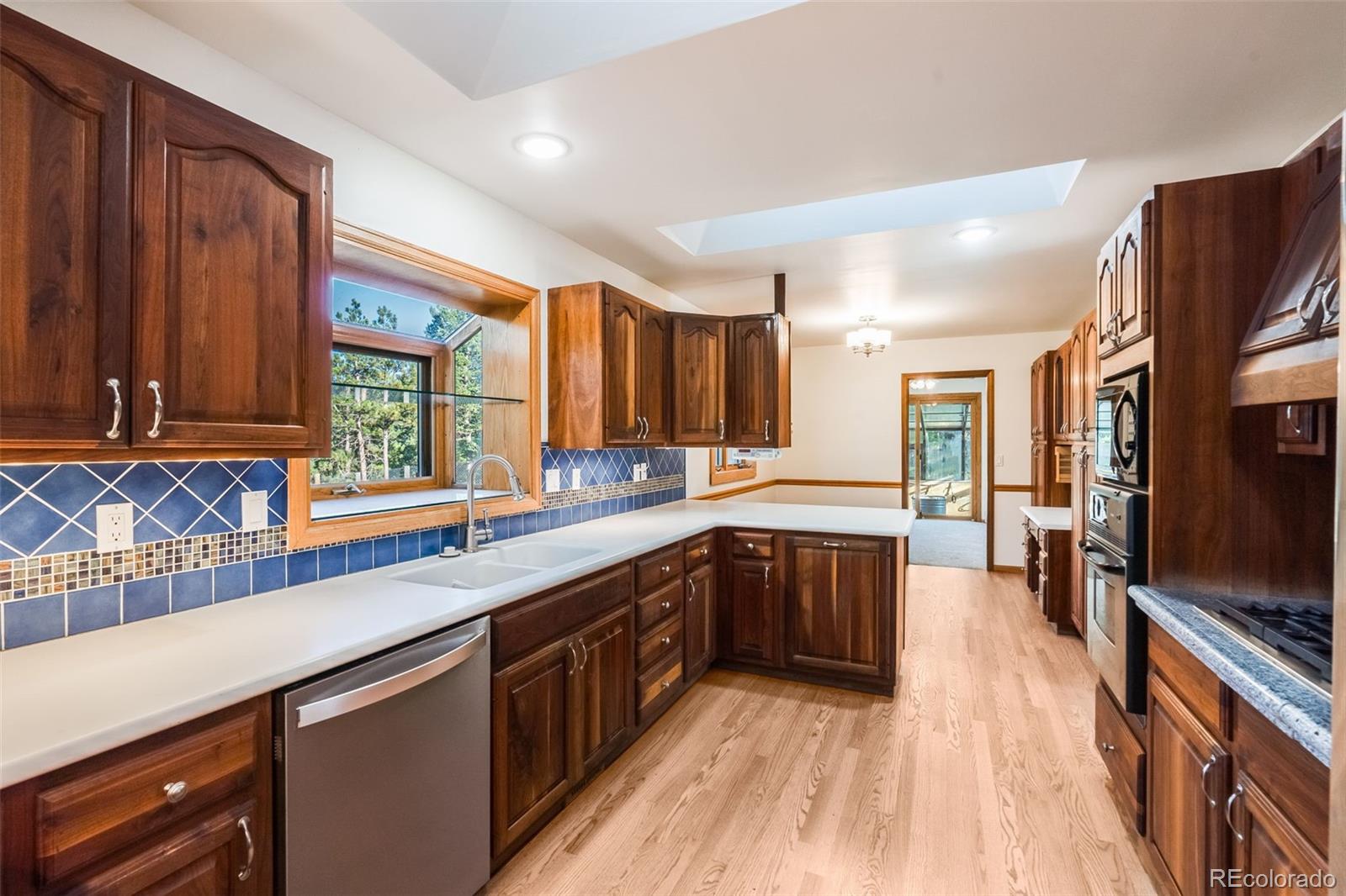 7572 Surrey Drive Morrison, CO 80465 - Photo 9 of 38 a kitchen with stainless steel appliances wooden floors wooden cabinets a sink and a window