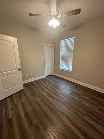an empty room with wooden floor chandelier fan and windows