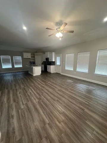 a view of an empty room with wooden floor and a kitchen