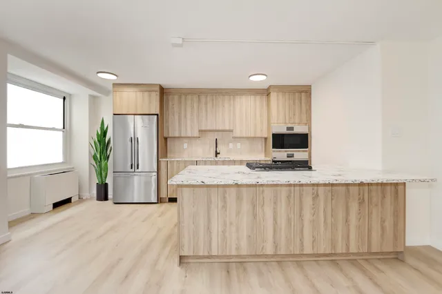 a kitchen with kitchen island granite countertop a refrigerator oven a sink dishwasher and white cabinets with wooden floor