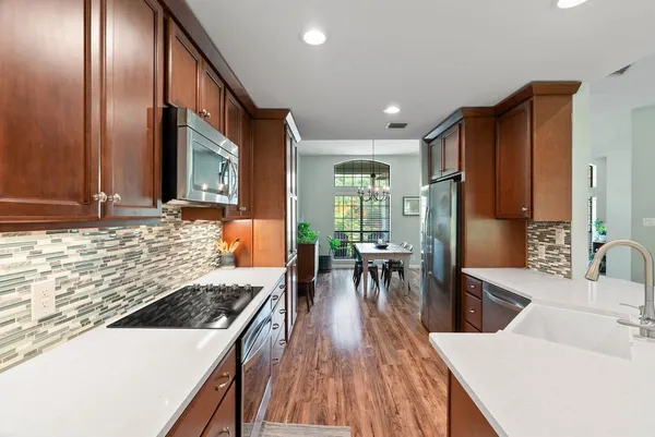 a kitchen with stainless steel appliances granite countertop a refrigerator a sink dishwasher a stove and a dining table with wooden floor