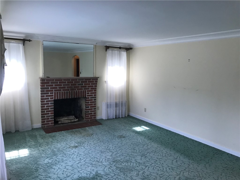 Living room with working brick fireplace. There are hardwoods under rug.
