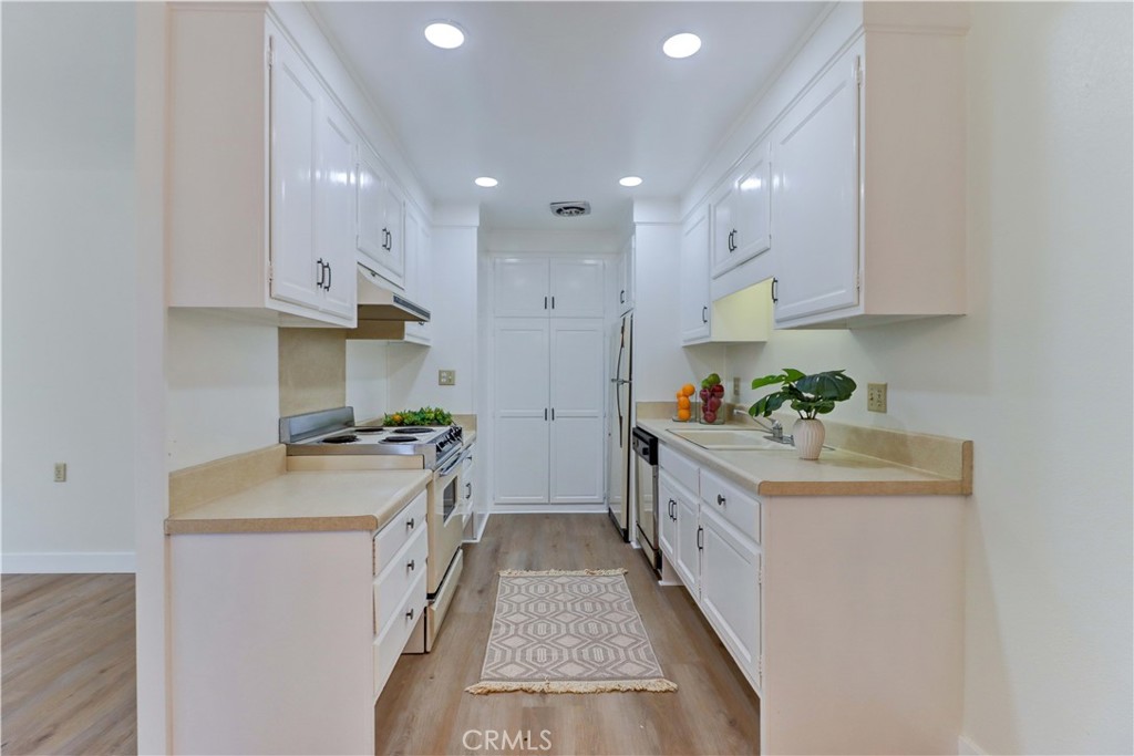 2123 Ronda Granada, Unit A Laguna Woods, CA 92637 - Photo 16 of 34 a kitchen with stainless steel appliances granite countertop a white stove top oven a sink and white cabinets with wooden floor