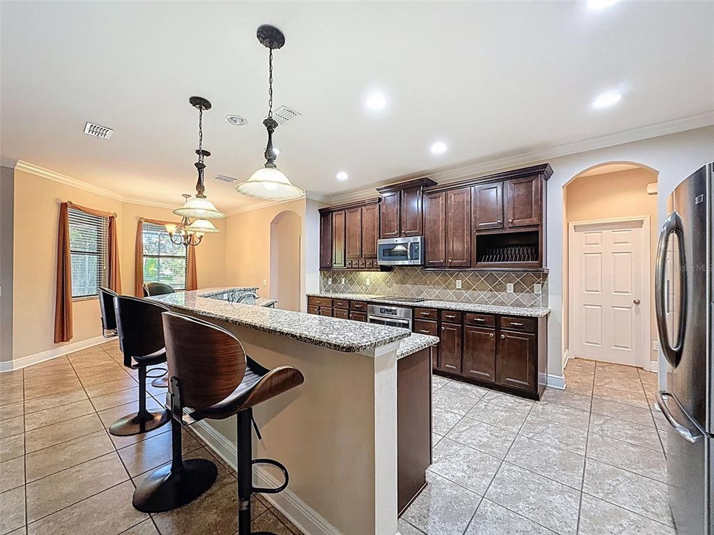 335 Cockle Shell Loop Apollo Beach, FL 33572 - Photo 16 of 90 a kitchen with stainless steel appliances granite countertop a stove top oven a refrigerator a sink and a dining table with wooden floor