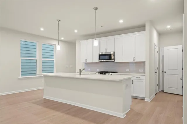 a kitchen with stainless steel appliances granite countertop a sink a stove a refrigerator and white cabinets