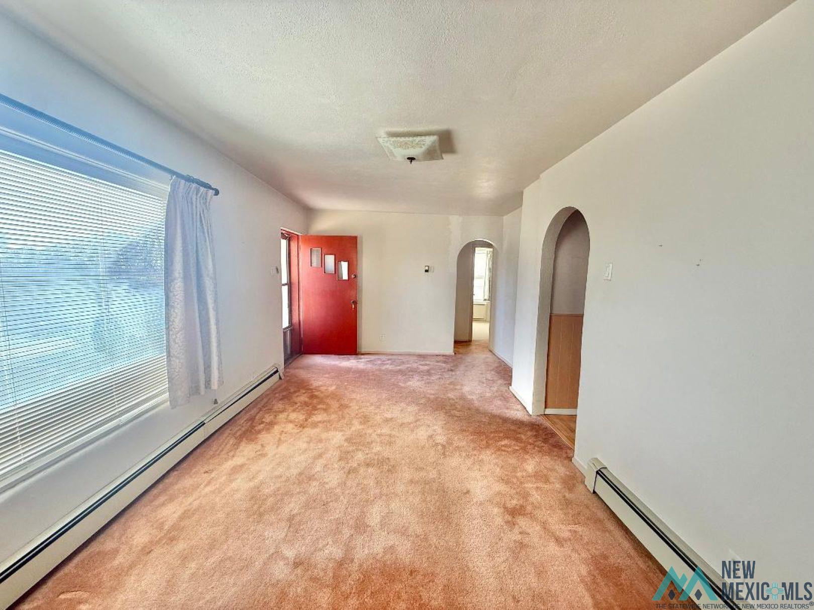904 South 4th Street Raton, NM 87740 - Photo 3 of 19 Spare room featuring a baseboard radiator, arched walkways, a textured ceiling, and light colored carpet