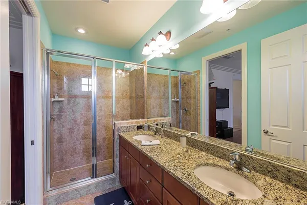 a bathroom with a granite countertop double vanity sink mirror and shower