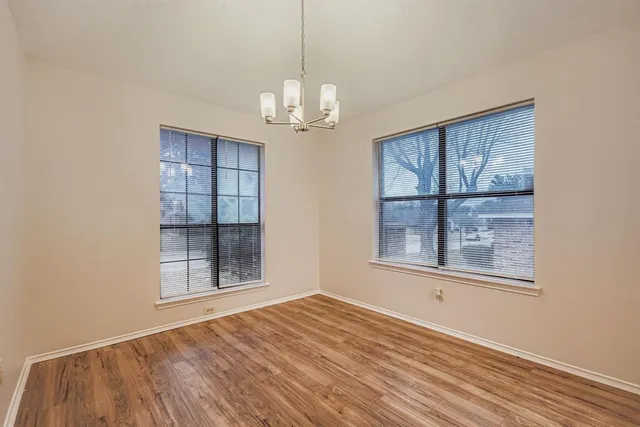 an empty room with wooden floor chandelier and windows