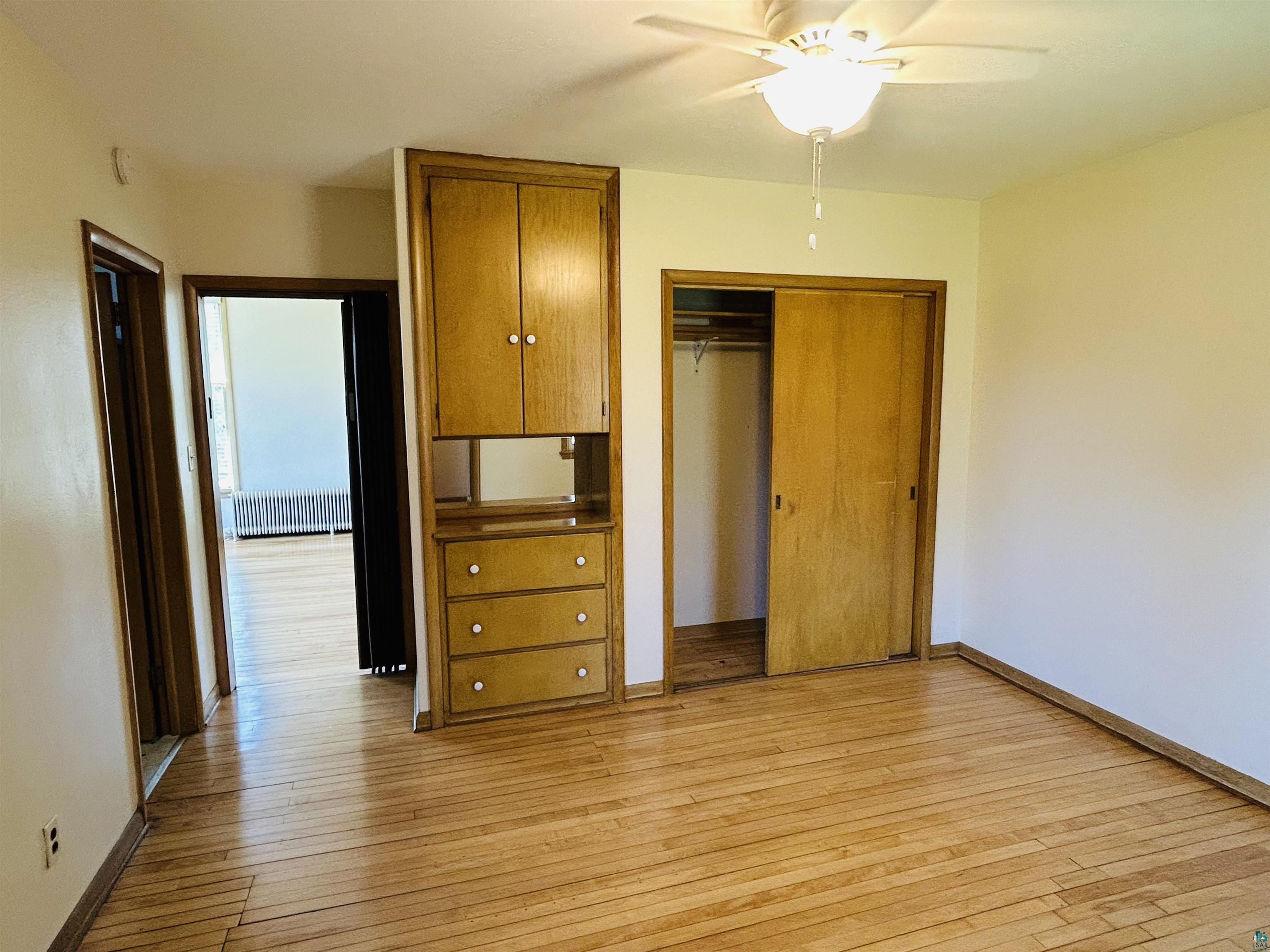 5090 London Road, Unit 1 Duluth, MN 55804 - Photo 29 of 54 Wood-finish flooring throughout, featuring a built-in wood cabinet with drawers, a sliding door closet, and a ceiling fan with integrated lighting