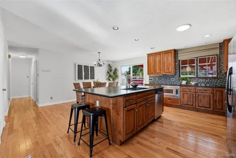a kitchen with stainless steel appliances granite countertop a refrigerator a stove a kitchen island a dining table and chairs with wooden floor