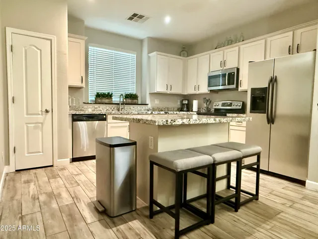 a kitchen with stainless steel appliances granite countertop a stove a refrigerator a sink a dining table and chairs with wooden floor