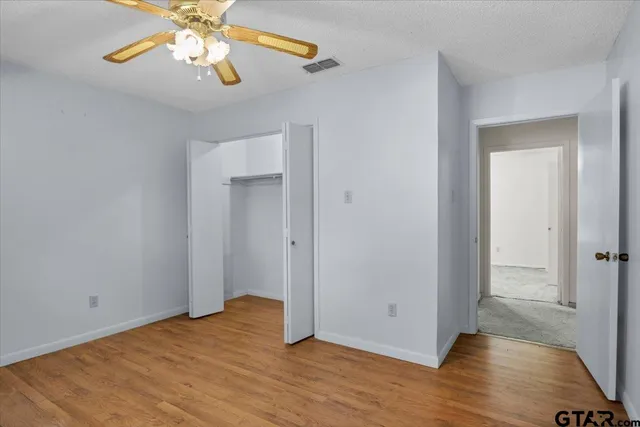 a view of an empty room with wooden floor and a ceiling fan