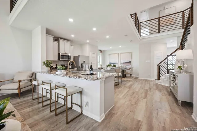 a kitchen with stainless steel appliances granite countertop a refrigerator a sink dishwasher a stove and a dining table with wooden floor