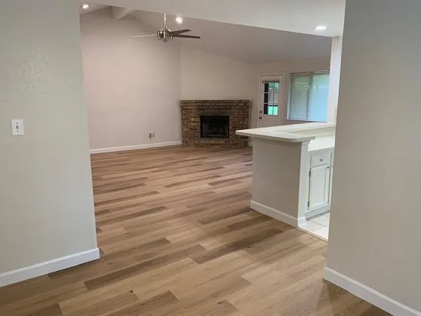 a view of an empty room with wooden floor and a kitchen