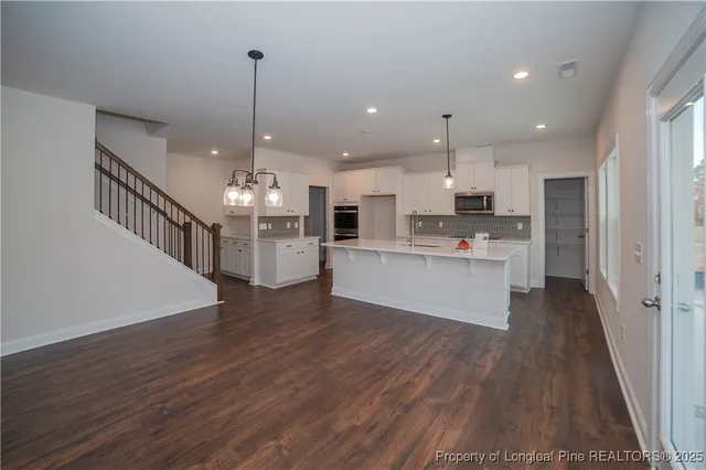 a large kitchen with kitchen island a stove a sink dishwasher a refrigerator and white cabinets with wooden floor