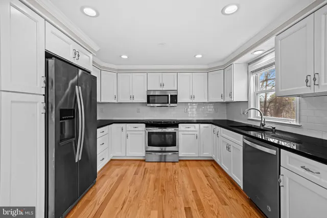 a kitchen with stainless steel appliances granite countertop a refrigerator a sink dishwasher a stove and white countertops with wooden floor